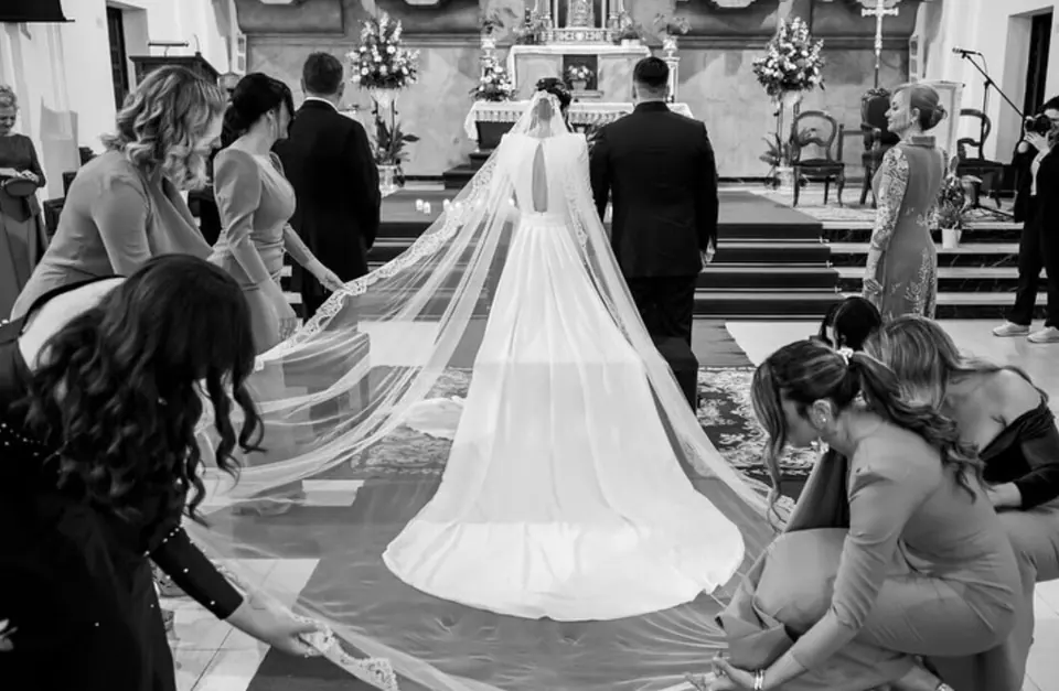 Novia de espaldas en el altar con un largo velo, en blanco y negro