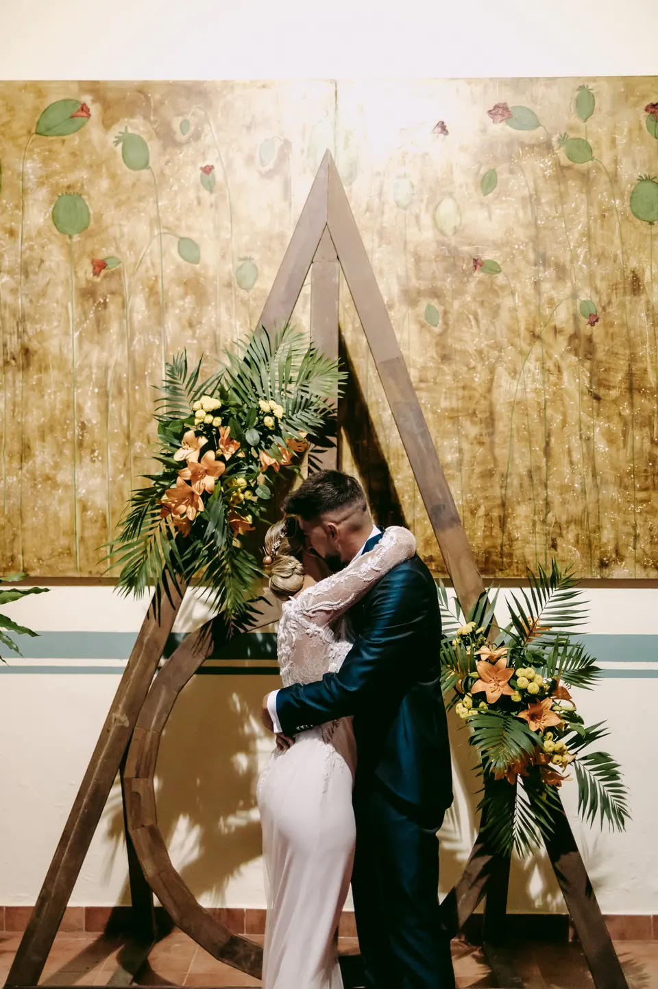 Los novios se besan bajo un arco de madera decorado con flores tropicales