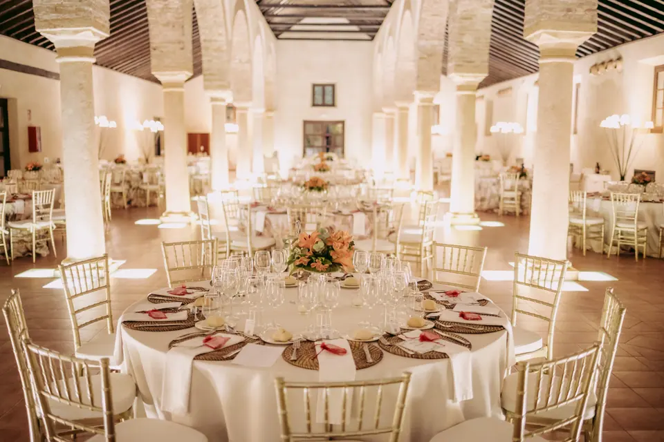 Salón de banquete montado con mesas redondas, mantelería blanca y centros de flores